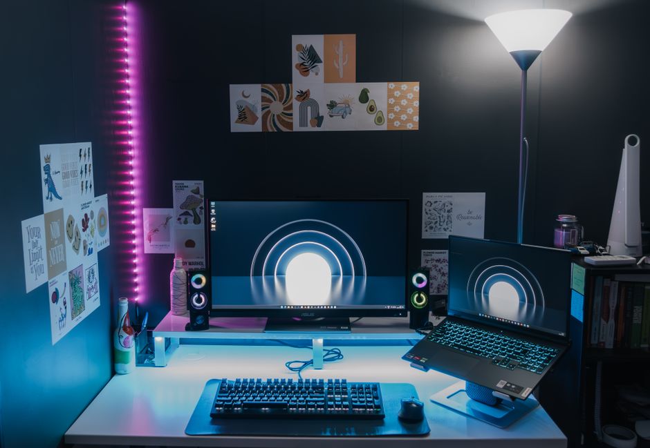 暗い部屋で明るい映像を映すモニターとノートPCのデスク