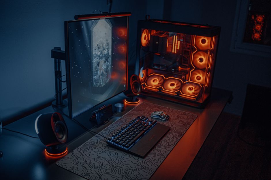 オレンジに光るファンを備えたデスクトップゲーミングPCとモニター、キーボードを置いたデスク