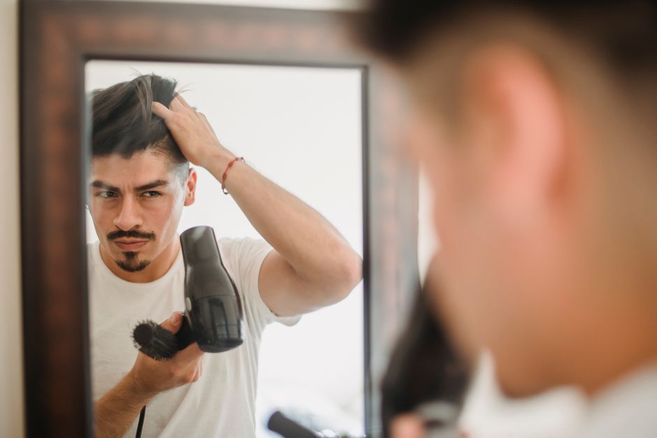 鏡の前でドライヤーを使いながら髪をセットする男性