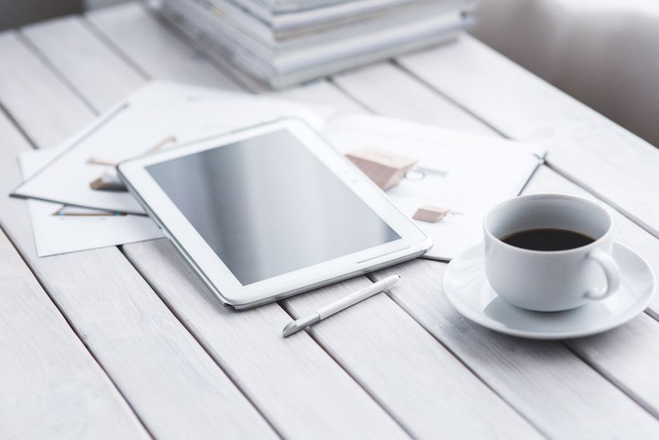 白いデスクに置かれたタブレットとスタイラスペン、コーヒーカップ