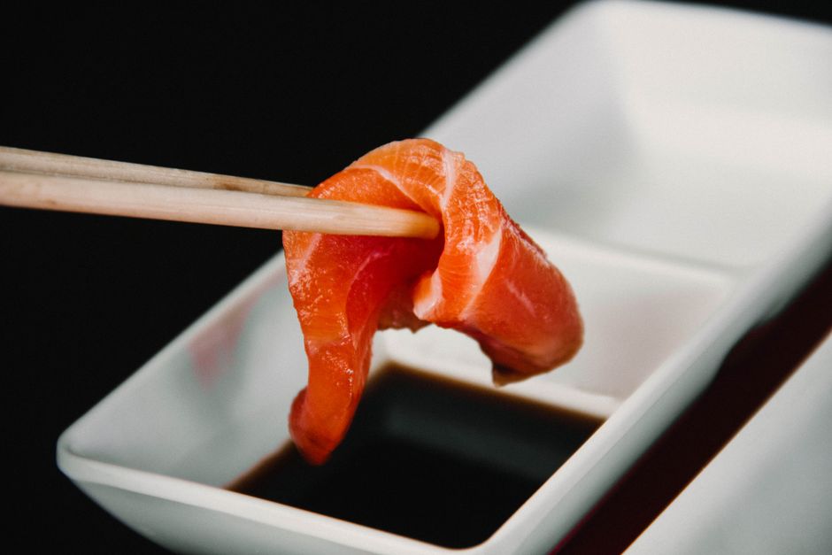 箸でつまんだサーモンの刺身を小皿の醤油につけるところ