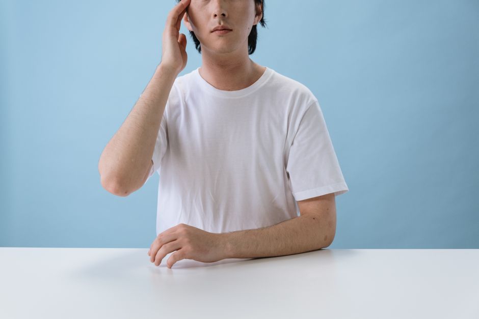 白いTシャツを着て青い背景の前に座る男性